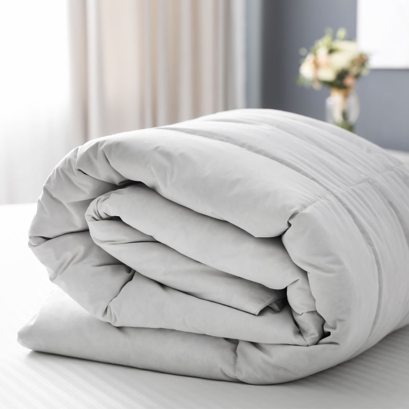 A folded cotton blend duvet displayed on a bed with a blurred background featuring a window and curtains.