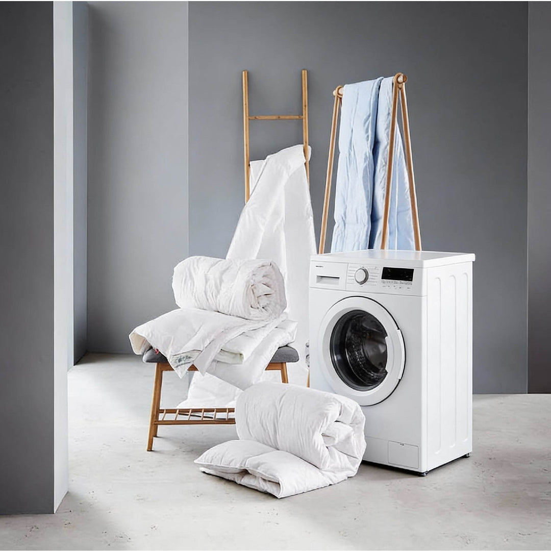 Laundry scene showing a white washing machine and a pile of clean white bedding.