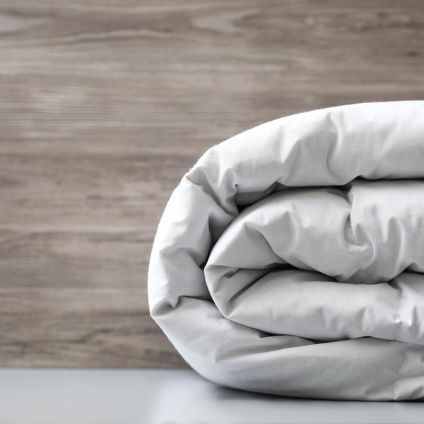 A rolled up white 9 tog cotton blend duvet displayed against a wooden background.