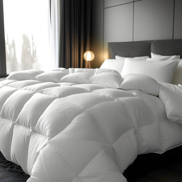 A luxury 13.5 tog Hungarian white goose feather & down duvet cover presented on a bed in a stylishly decorated room with a lamp and curtains in the background.